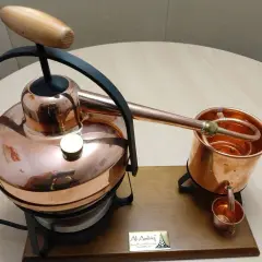 Miedziany alembik z drewnianą rączką, gotowy do pracy.
