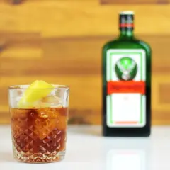 Orzeźwiający jager z colą, z plasterkiem cytryny, obok zielonej butelki Jägermeistera.