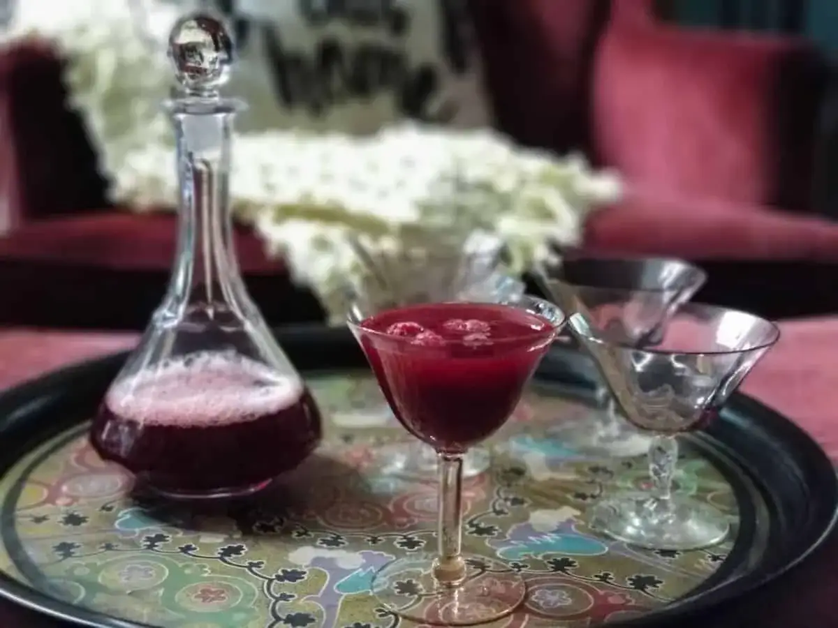 Elegancki karafka i kieliszek z rubinowym cordial drink, ozdobione malinami.