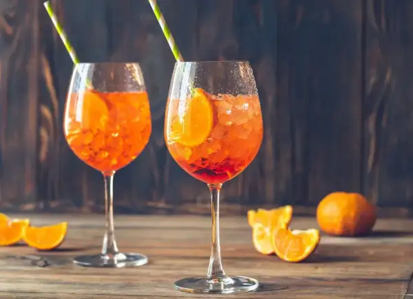 Dwa orzeźwiające drinki orange spritz z plasterkami pomarańczy i słomkami, na drewnianym stole.